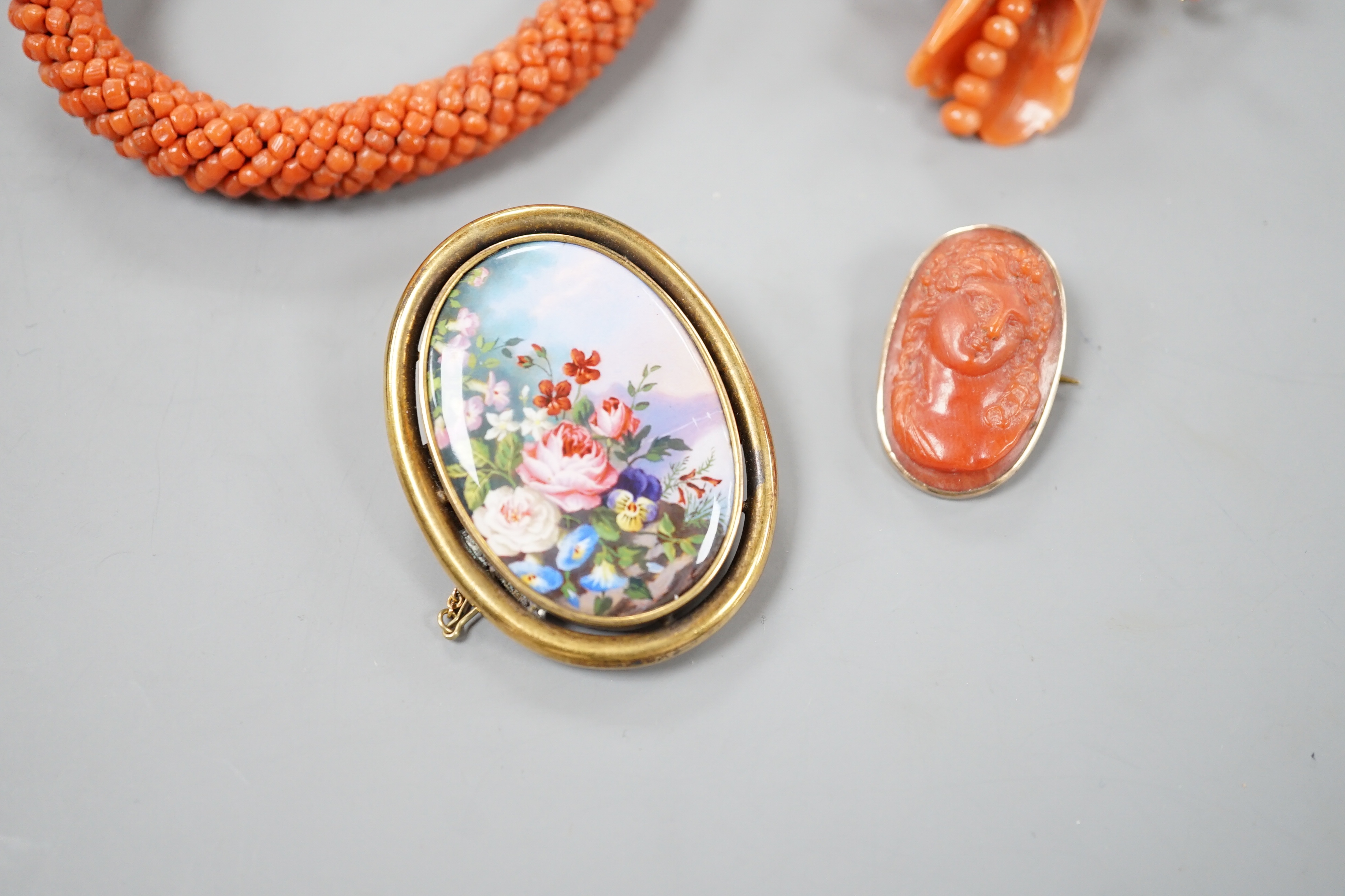 A yellow metal mounted carved coral oval brooch, 30mm, a mounted coral open bangle, a coral brooch and a gilt metal and enamelled brooch.